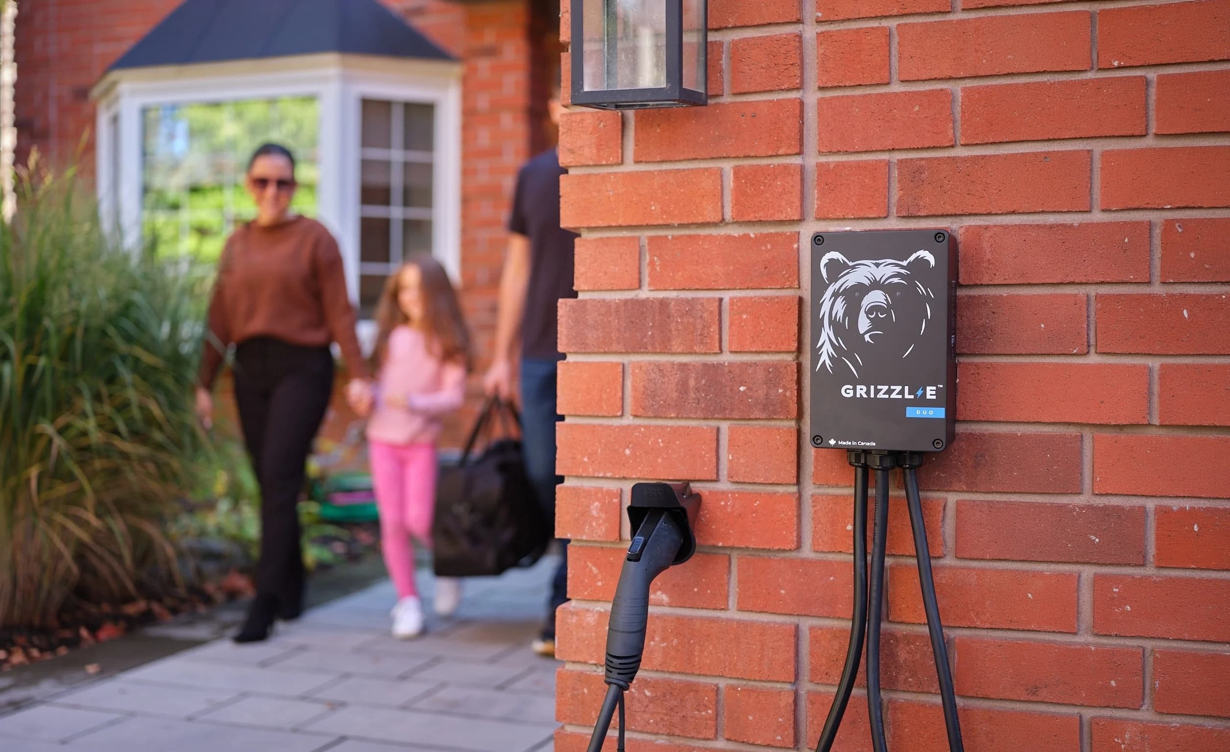 A family walking home past a Grizzl-E Duo charger mounted on a brick wall