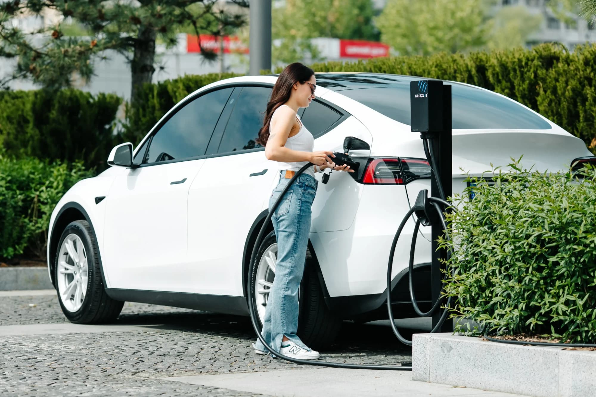 A woman plugging a white electric SUV into a pedestal-mounted Grizzl-E charger
